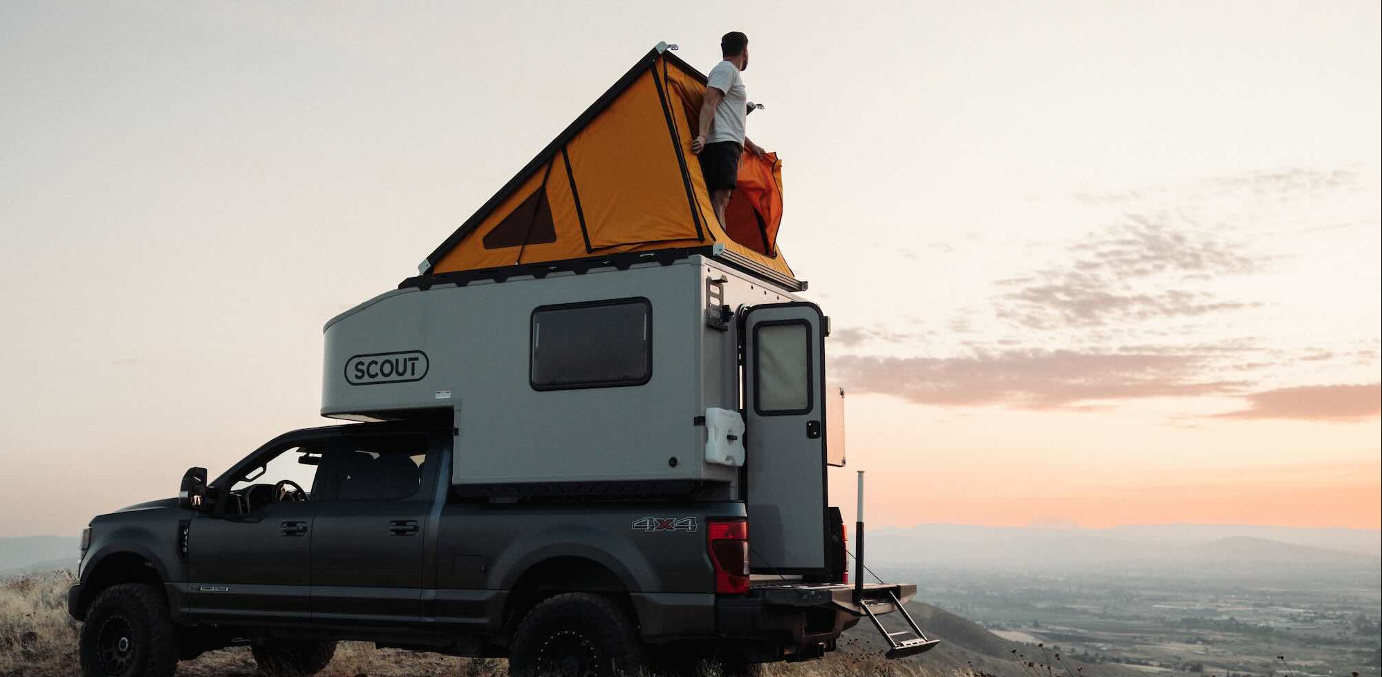Scout truck camper with a person standing on the roof at sunset