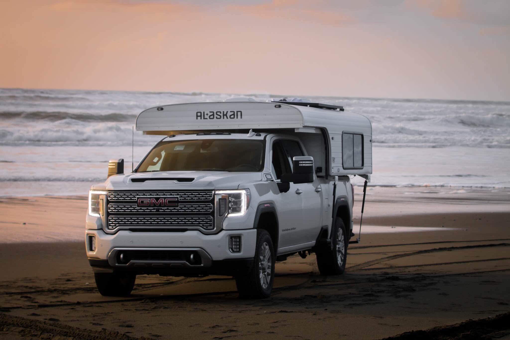 White truck with a white Alaskan slide-in cabover camper on a beach at sunset