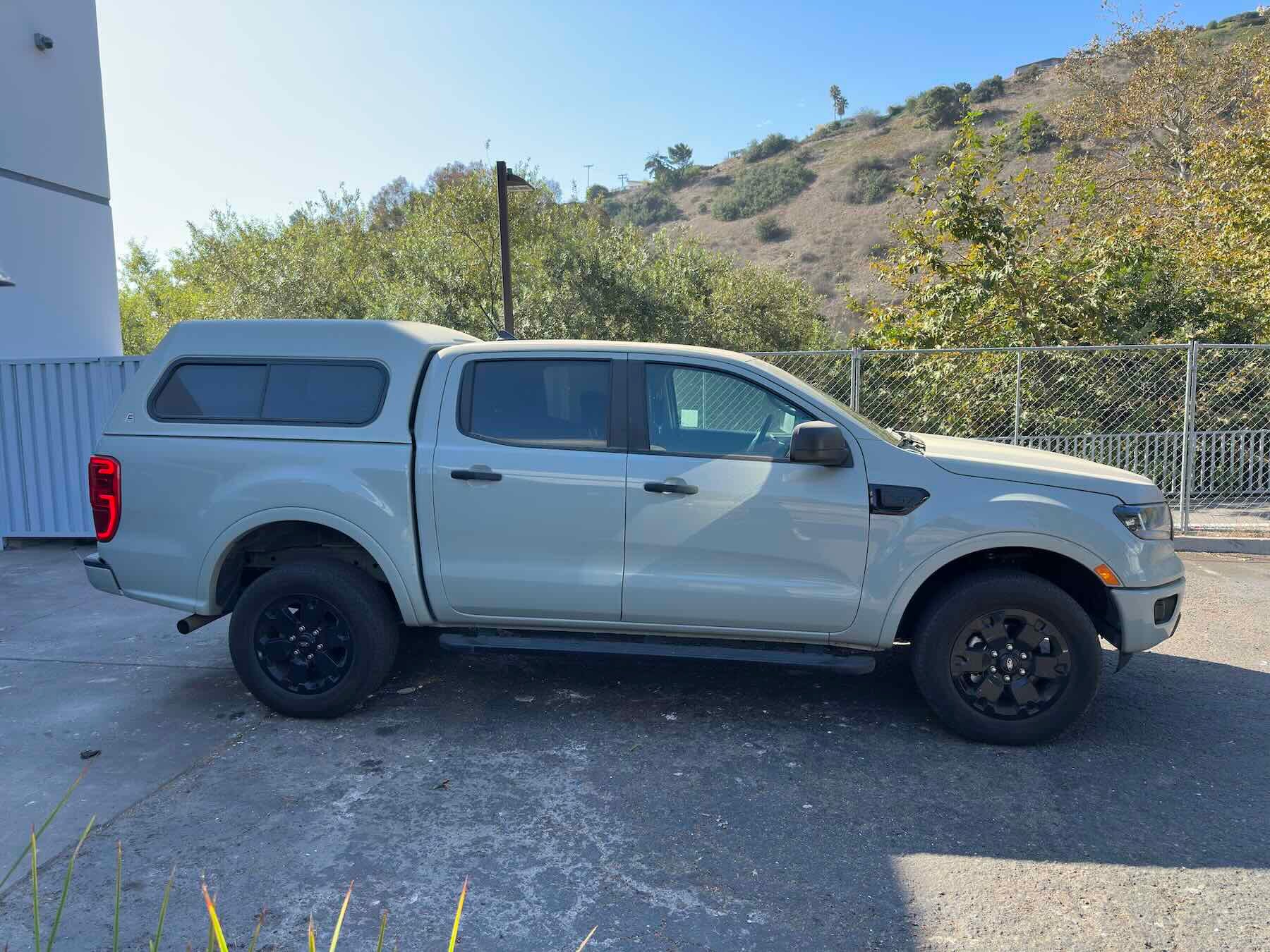 Grey Ford Ranger parked in a log with grassy hill in background