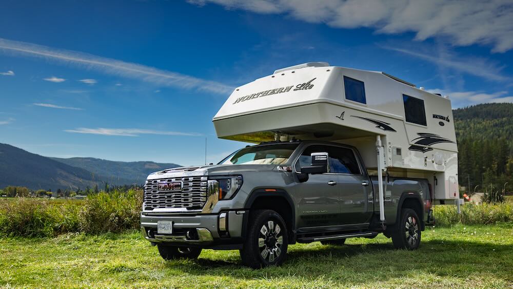Dark grey pickup truck with white northern lite slide in truck camper in bed parked on green grass