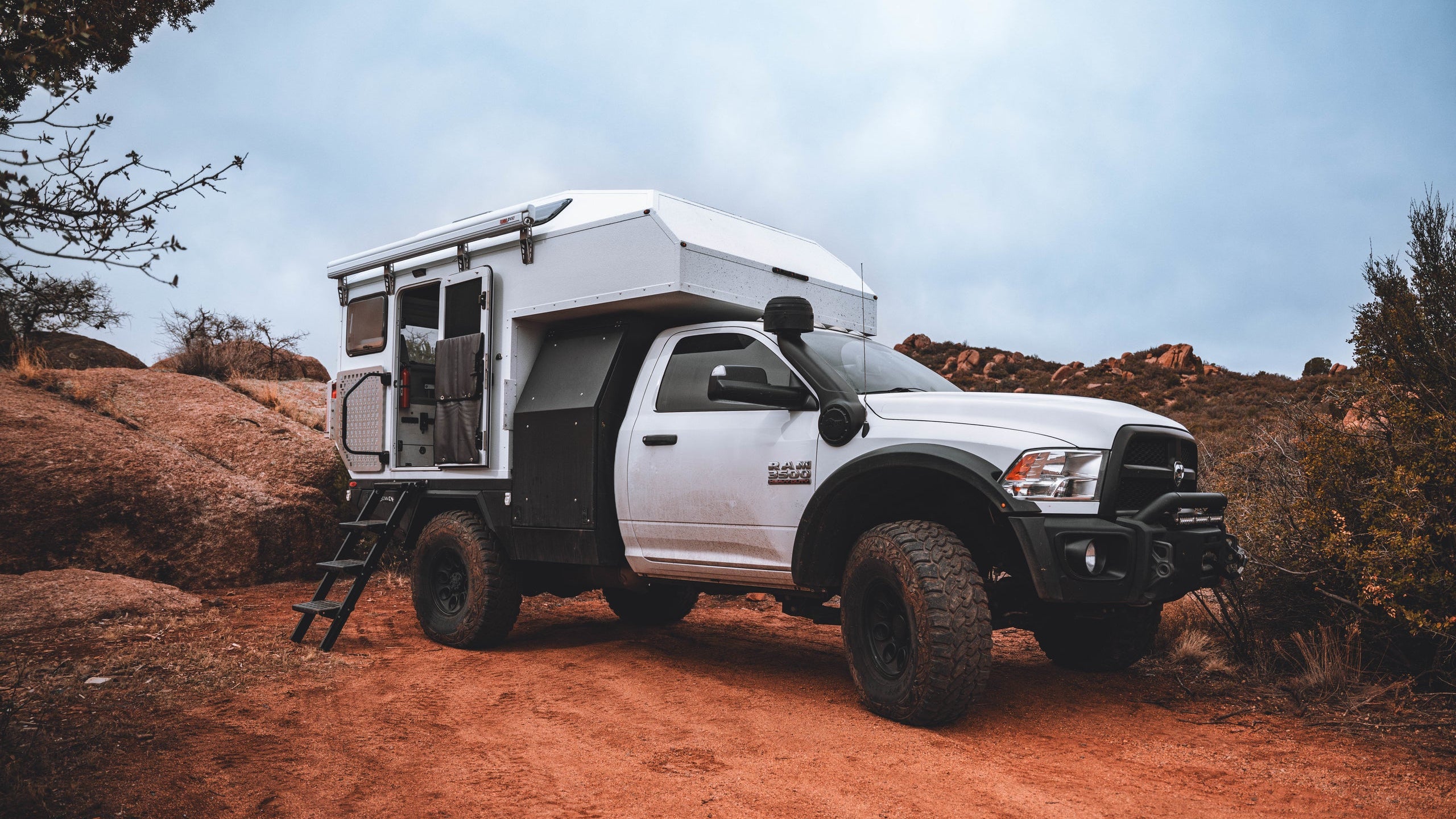 White truck with AT Overland Aterra camper shell on a dirt road in a desert landscape
