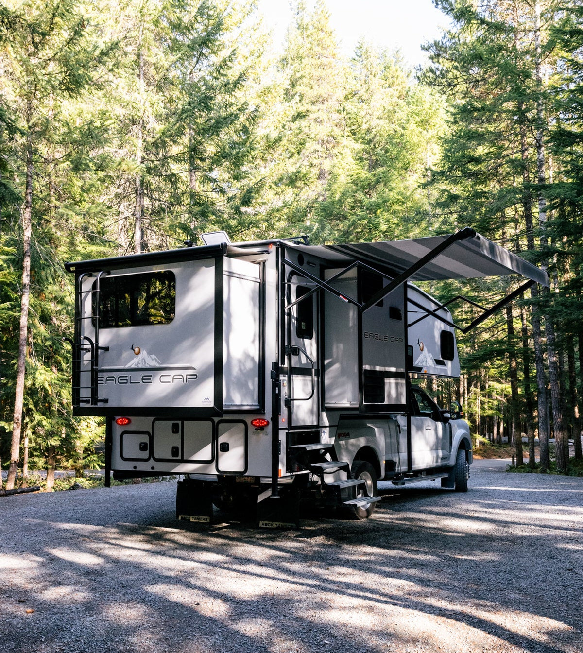 Hard side truck camper set up at a shaded forest campsite