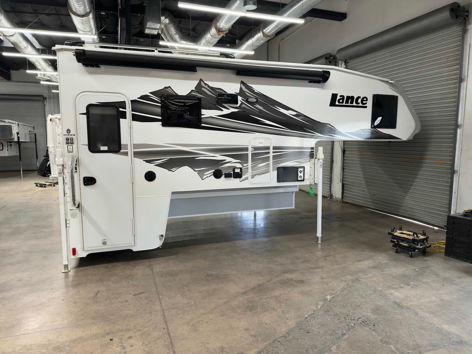 Exterior of white Lance 1191 truck camper with black and grey graphics resting on its corner jacks in a garage