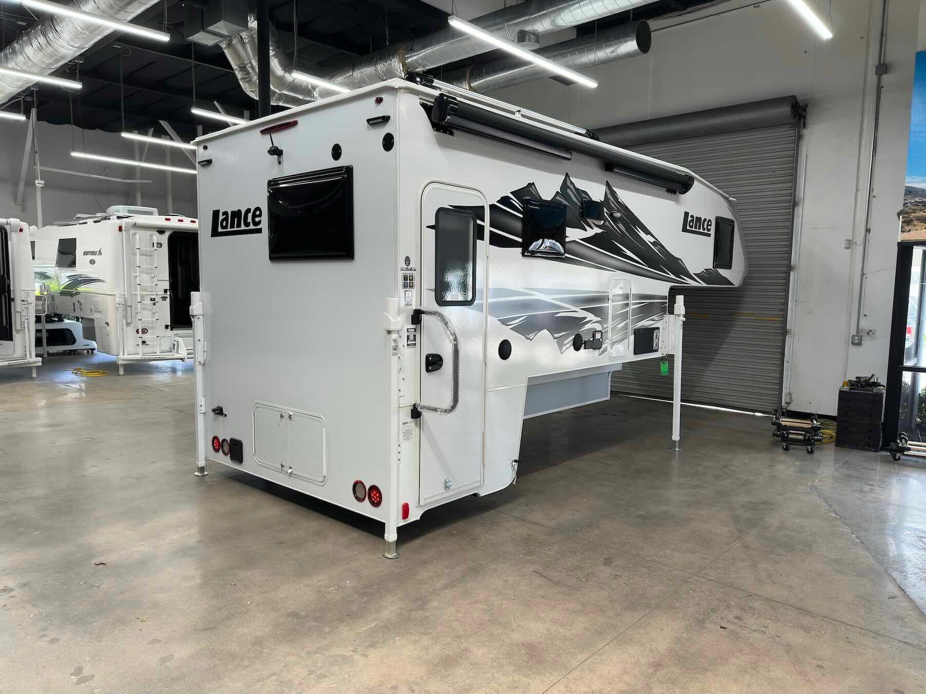 Exterior of white Lance 1191 truck camper in a showroom setting showing side awning and side entry