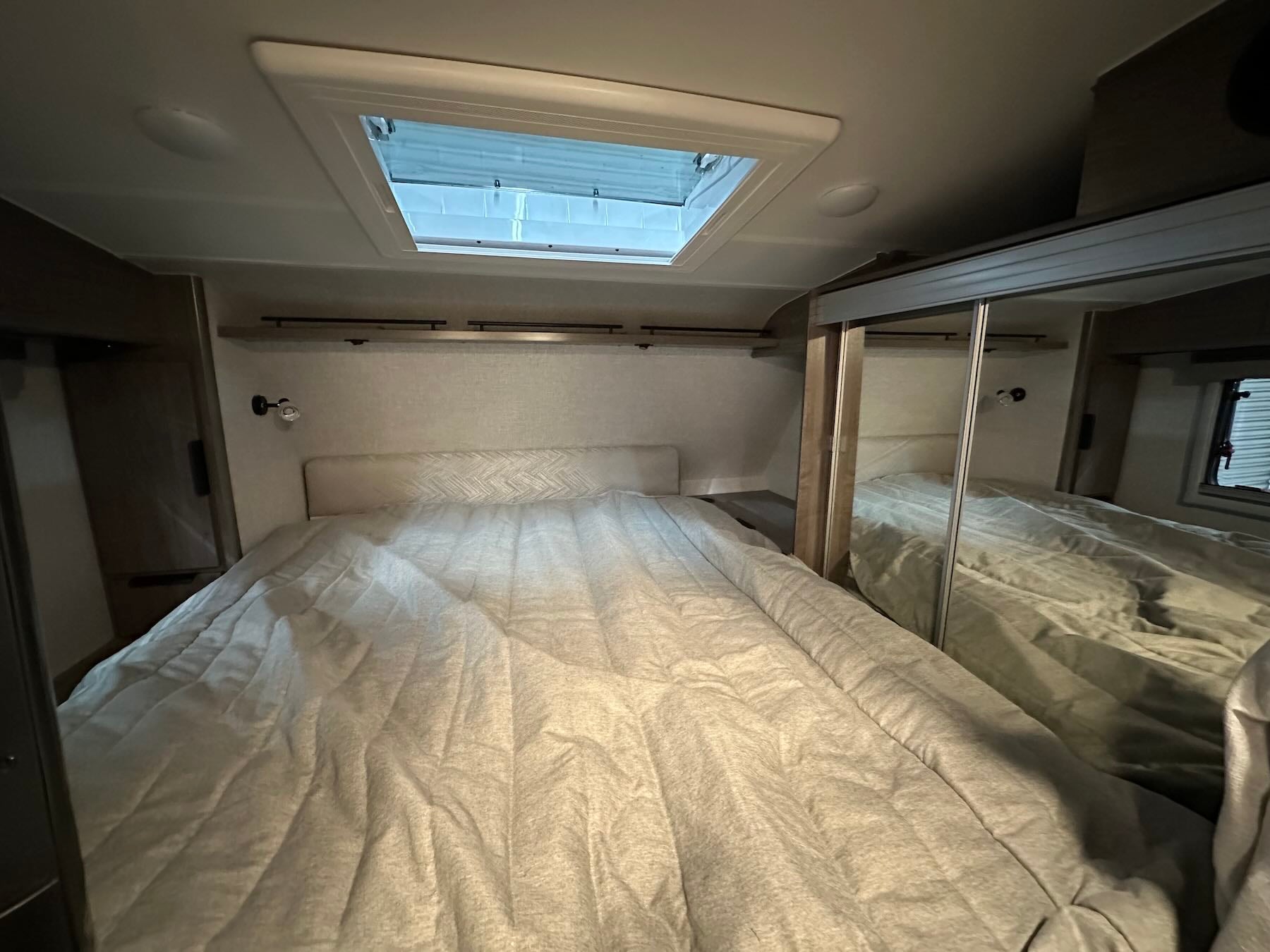 Interior of bed area inside Lance 1191 showing a bed, mirrored cabinets, and skylight.