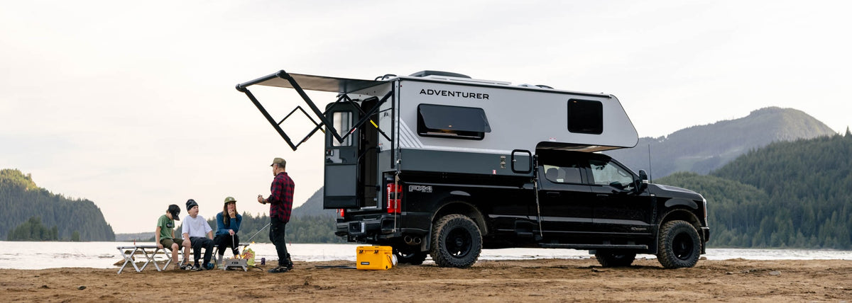 A loaded truck camper rig parked in the mountains with people sitting outside