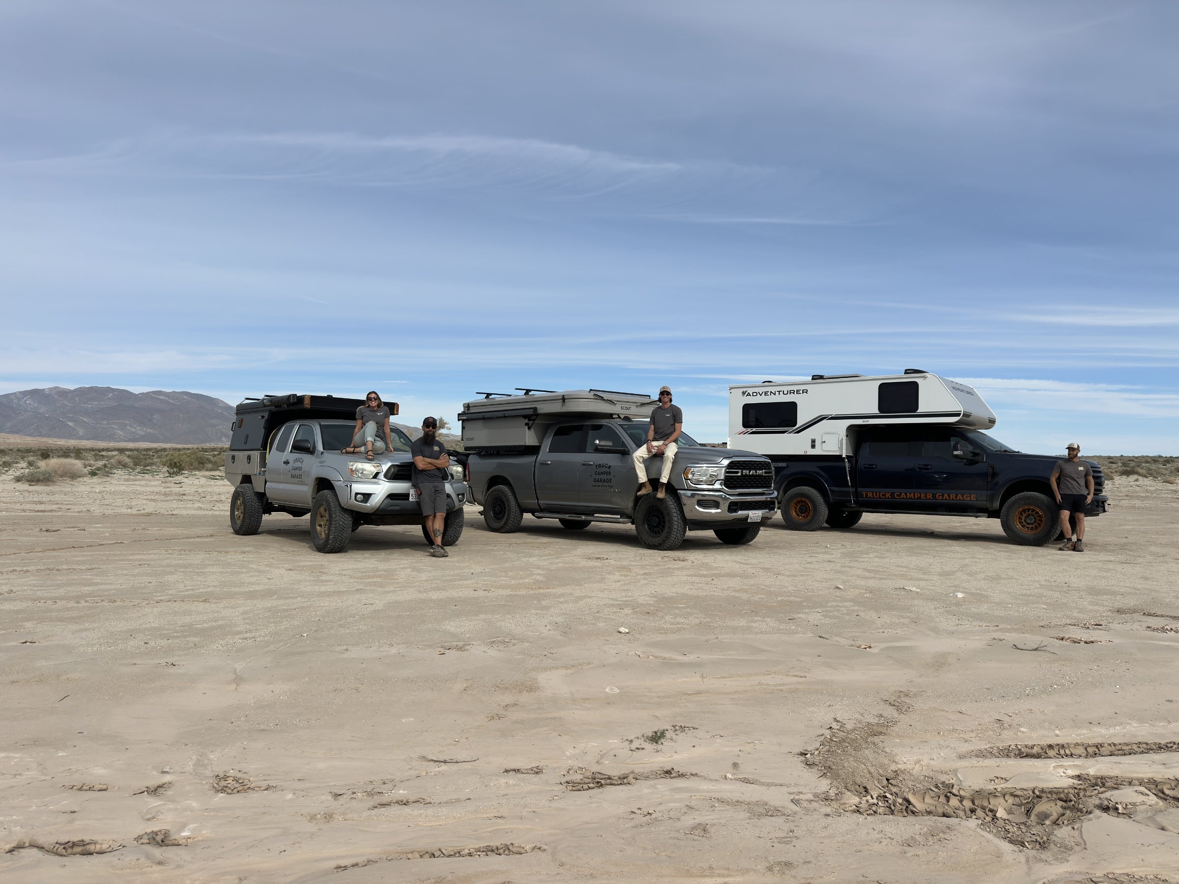 The three male TCG owners and a female partner standing next to their truck camper rigs in the desert