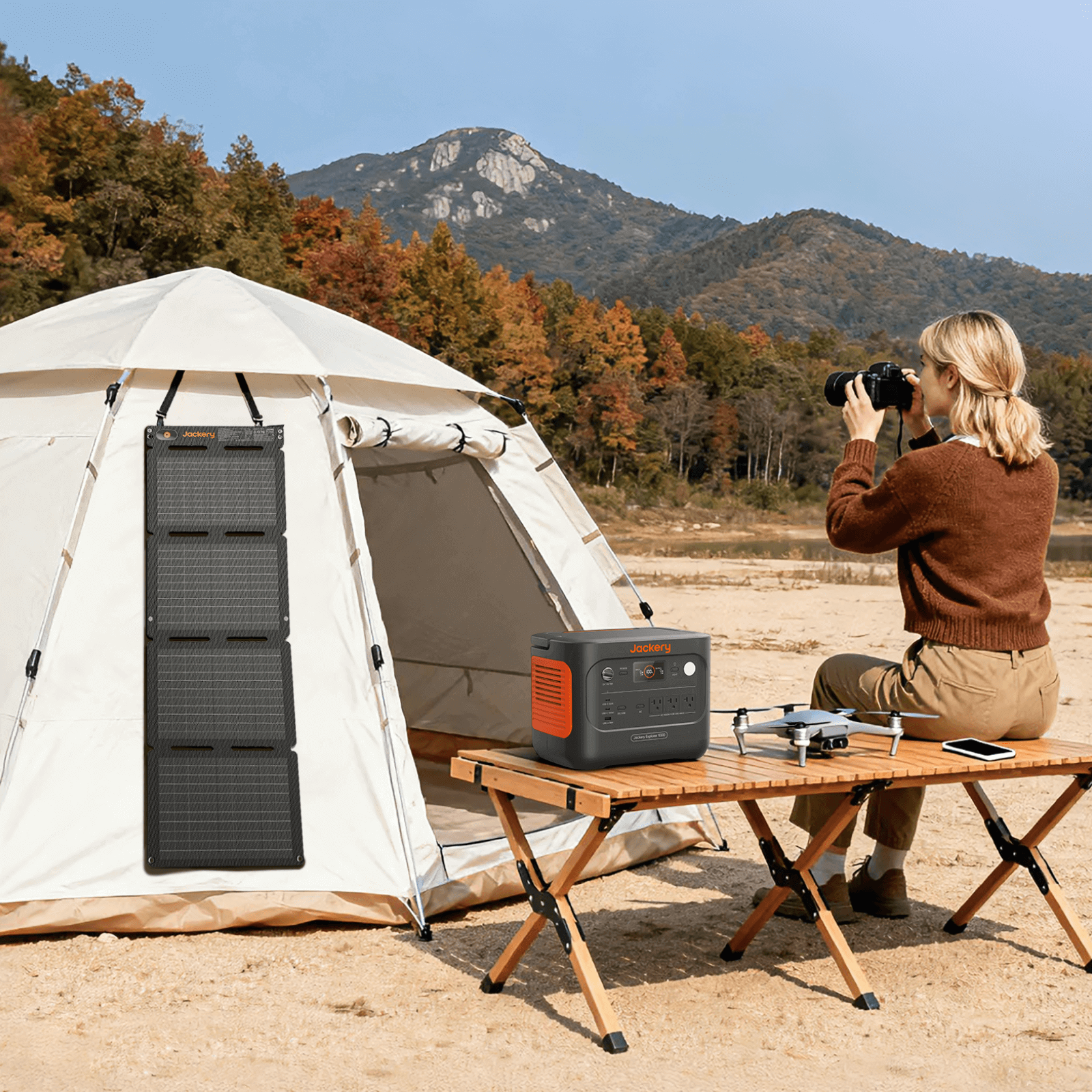 Person taking a photo of a tent with a portable power station and solar panel in a scenic outdoor setting.